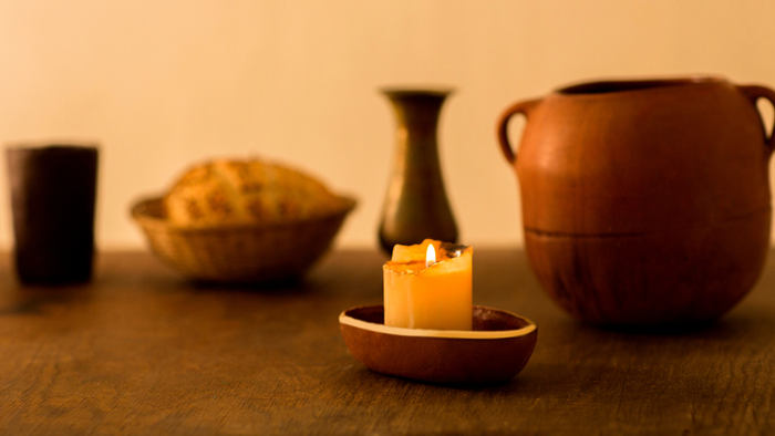 Gemütlicher Holztisch mit einer brennenden Kerze, einer Keramikschale, einem Krug und einer dunklen Tasse.