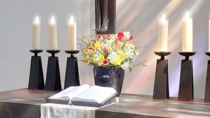 Zwei Kerzenleuchter mit weißen Kerzen und eine Vase mit bunten Blumen auf einem Tisch