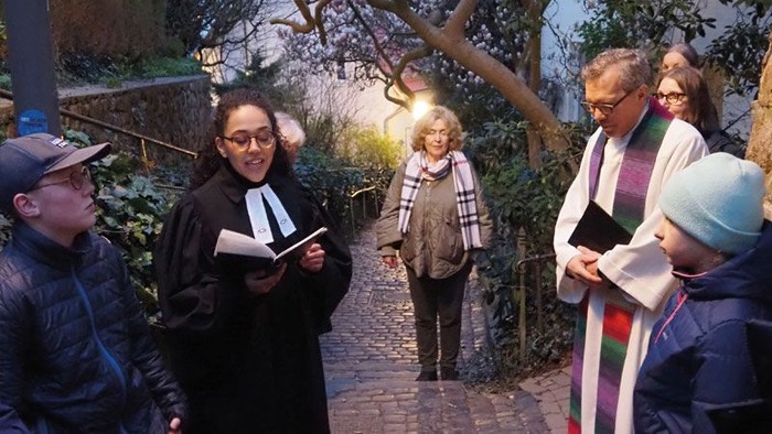 Gruppe von Menschen, darunter Geistliche, die bei Einbruch der Dämmerung im Freien spazieren, Bücher tragen und sich in der Nähe eines Gartenwegs unterhalten.