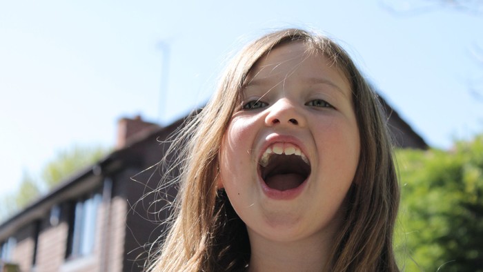 Et glade barn med lang blond hår åbner mundet vidt.