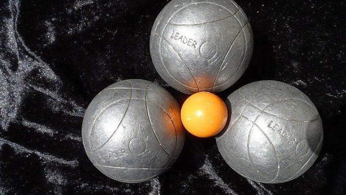 Kugeln für Pétanque, angeordnet um eine zentrale orange Zielkugel auf einer strukturierten Spielfläche.