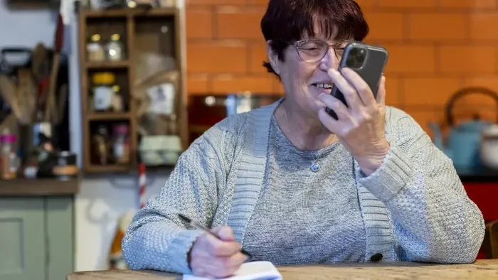 Eine ältere Frau telefoniert in der Küche und schreibt etwas auf.