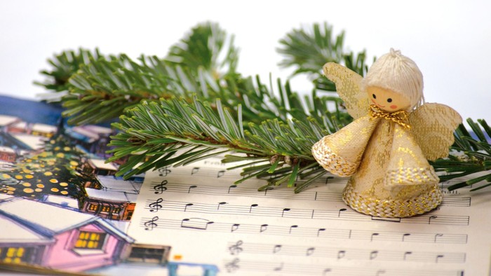 Eine kleine Engelurfigur sitzt auf einem Notenblatt, in der Nähe liegt ein Tannenzweig.