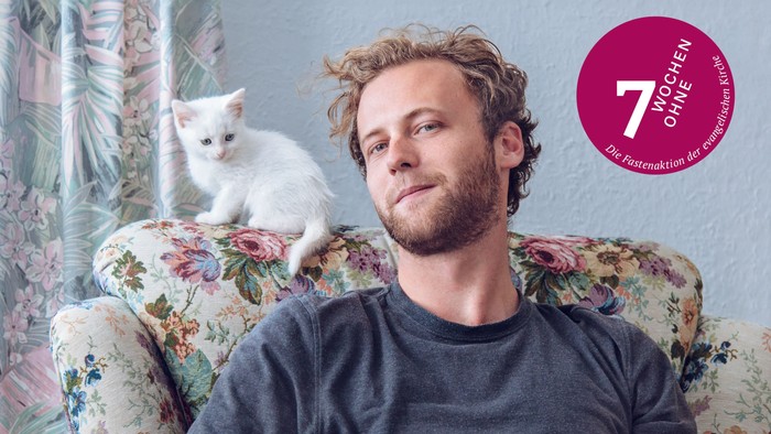 Das Aktionsmotiv 2026 der Fastenaktion 7 Wochen ohne: Ein Mann auf einem geblümten Sessel. Auf der Lehne sitzt eine weiße Katze.