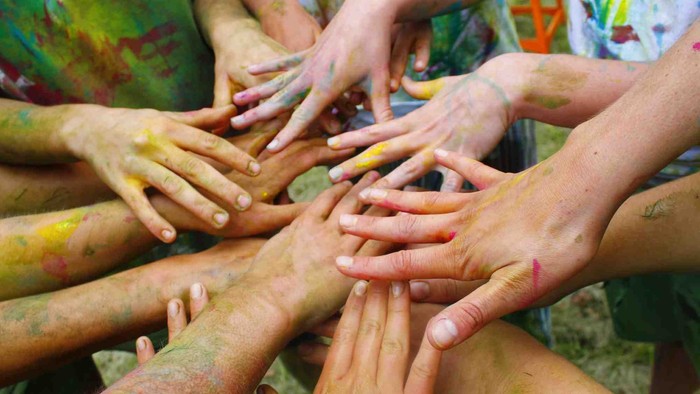 Bunte Hände, die in einer Gruppe zusammengefügt sind, bedeckt mit leuchtendem Pulverfarbenstaub.