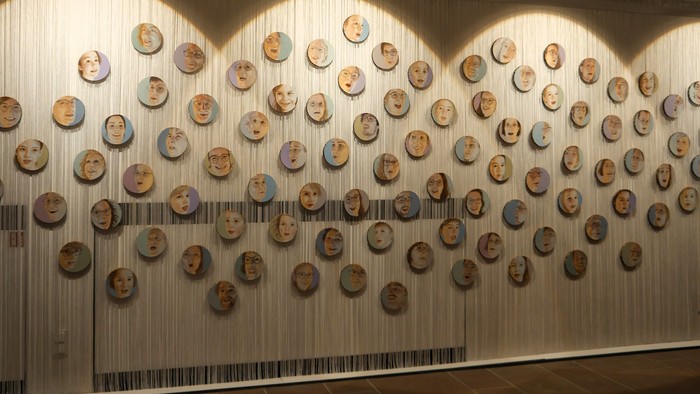 Kreative Wandkunst mit zahlreichen runden Knöpfen mit bemalten Gesichtern und Mustern in einer geschwungenen Anordnung.