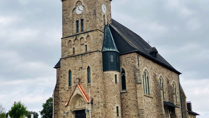 Historische Steinkirche mit Uhrturm und gewölbtem Eingang, vor bewölktem Himmel.