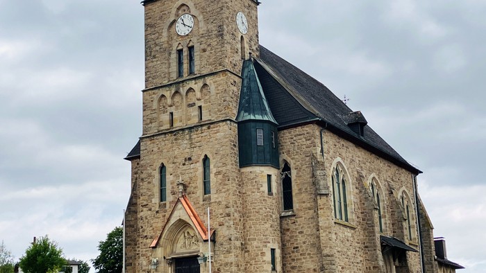 Historische Steinkirche mit Uhrturm und gewölbtem Eingang, vor bewölktem Himmel.