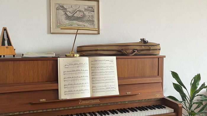 Elegantes Holzklavier mit Notenblättern, gerahmten Kunstwerken und einer kleinen Topfpflanze in der Nähe.