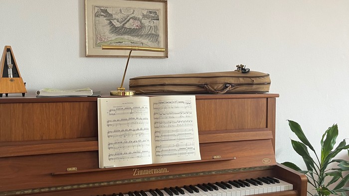 Elegantes Holzklavier mit Notenblättern, gerahmten Kunstwerken und einer kleinen Topfpflanze in der Nähe.