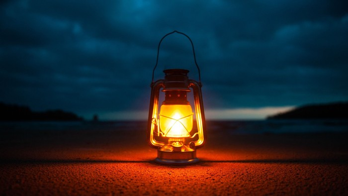 Et ensomt lygte kastede varmt lys på en mørk, tekstureret overflade under en stemningsfuld nattehimmel.