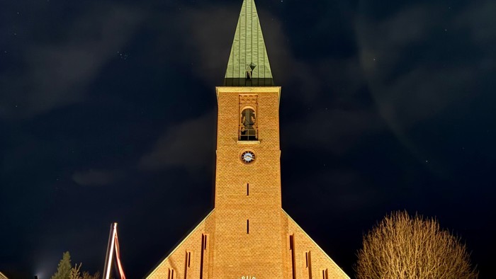 En smukt oplyst kirke med et klokketårn og slørede billygter mod en nattehimmel.