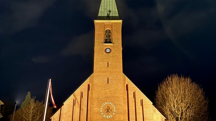 En smukt oplyst kirke med et klokketårn og slørede billygter mod en nattehimmel.