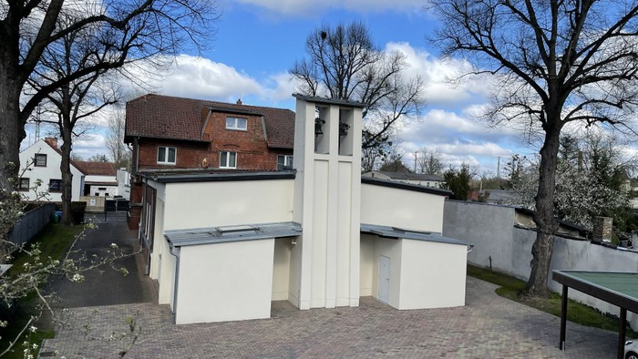 Modernes weißes Gebäude mit einzigartiger Architektur, umgeben von Bäumen und anderen Häusern.