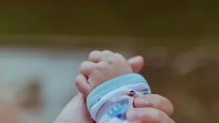 Eine Nahaufnahme von den winzigen Füßen eines Babys mit einer bunten Socke und einem blauen Armband.