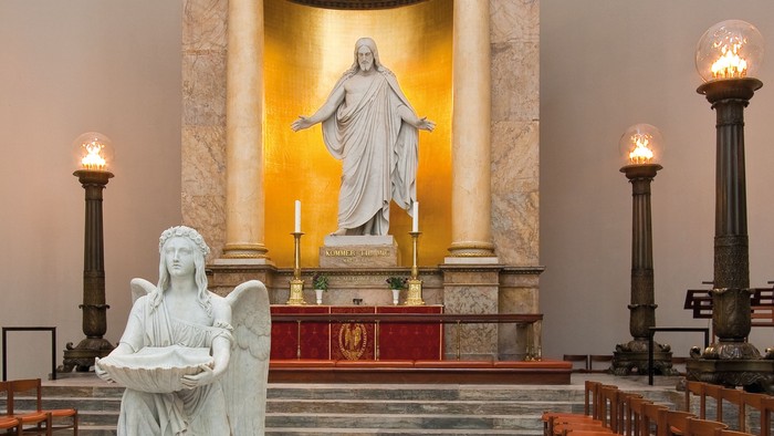 Elegant kapelinteriør med klassiske statuer, gyldent alterbaggrund og tændte lysestager.