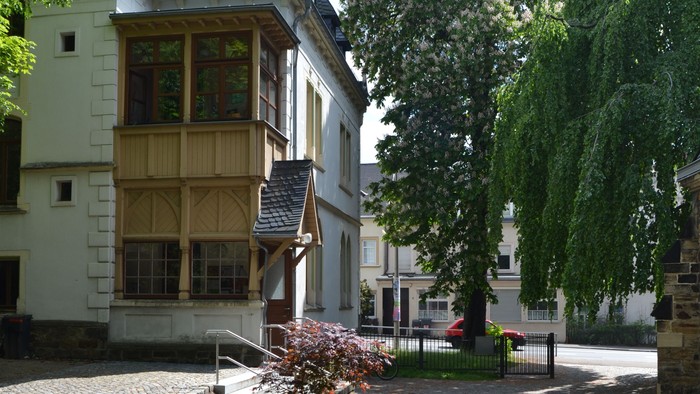 Ein Kopfsteinpflasterweg führt zu einem zweistöckigen Gebäude mit Balkon.