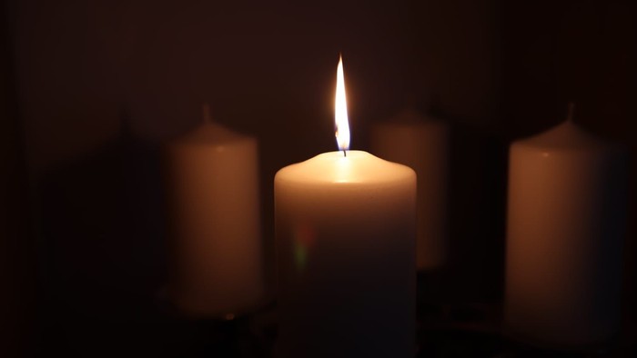 Drei Kerzen, eine angezündet, im Dunkeln.