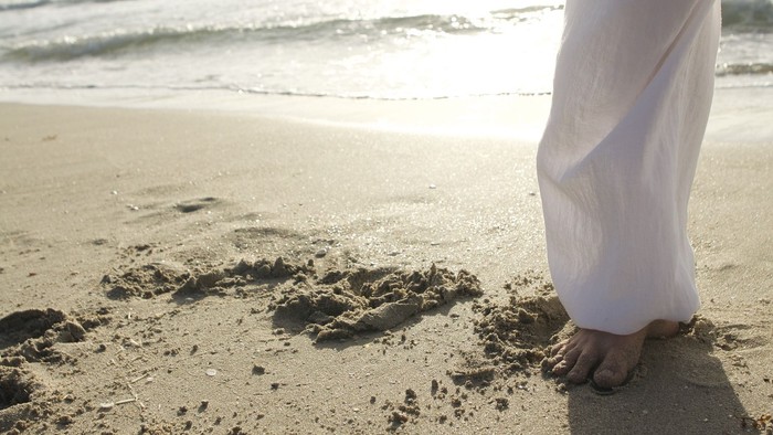 Person steht am sandigen Strand, Fußabdrücke sichtbar