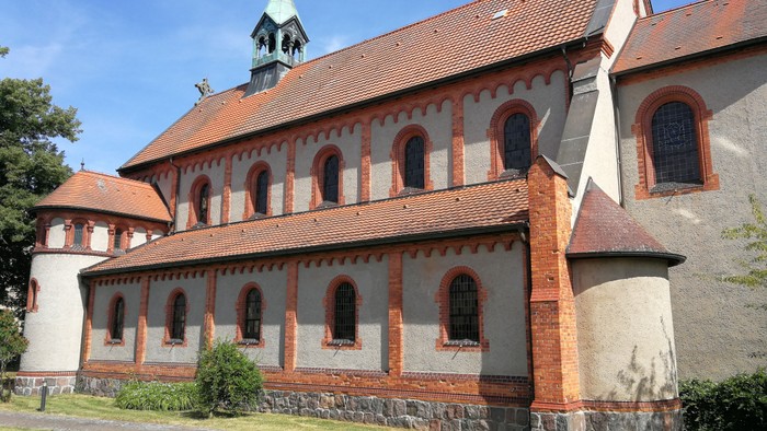 Das Bild zeigt eine rote Backsteinkirche mit weißem Putz und grünem Turm.