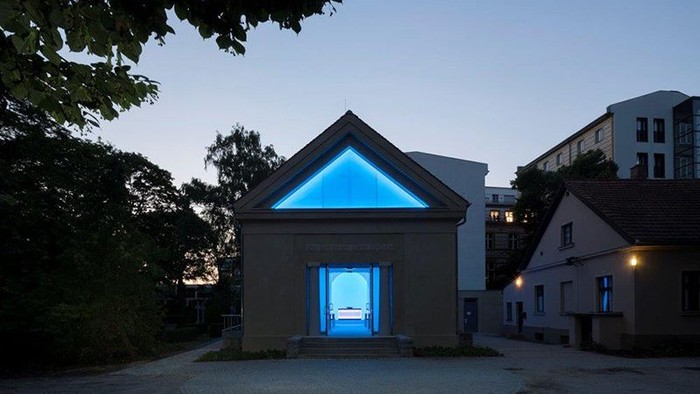 Ein modernes Gebäude mit blauer Beleuchtung in der Dämmerung, umgeben von Bäumen und anderen Strukturen.