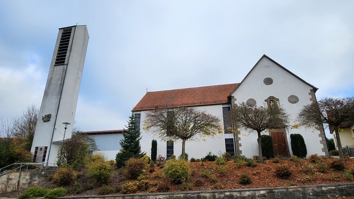 Weiße Kirche mit hohem Turm und rotem Dach, umgeben von Bäumen und Büschen