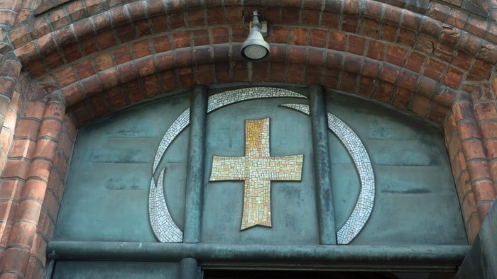 Das Bild zeigt den Eingang einer Kirche mit einem Kreuz über der Tür.