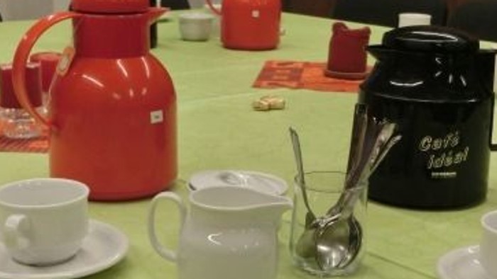 Auf dem Tisch stehen zwei Teekannen, Tassen und Utensilien auf einem grünen Tischtuch.