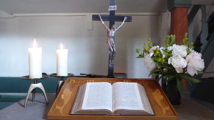 Heiliger Altaraufbau mit einer geöffneten Bibel, Kerzen, einem Kruzifix und einem Blumengesteck.