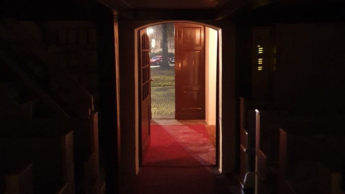 Dunkler Flur mit rotem Teppich, der zu offenen Holztüren führt.