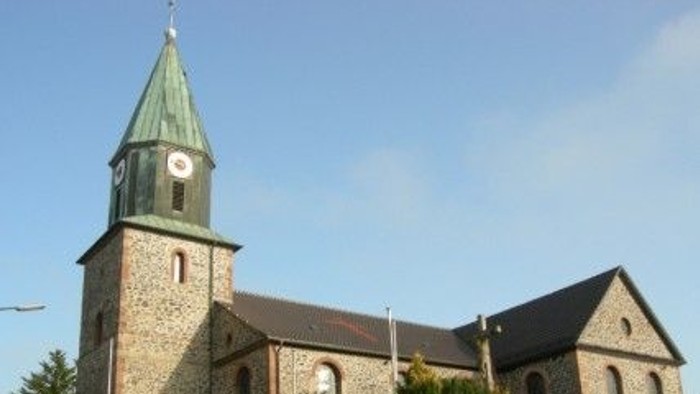 Steinkirche mit hohem Uhrturm und grünem Spitzturm vor klarem blauem Himmel.