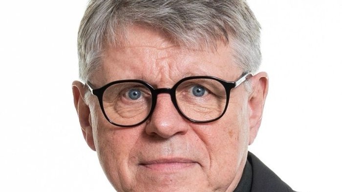 Et professionelt portræt af en ældre mand iført briller og en mørk blazer.