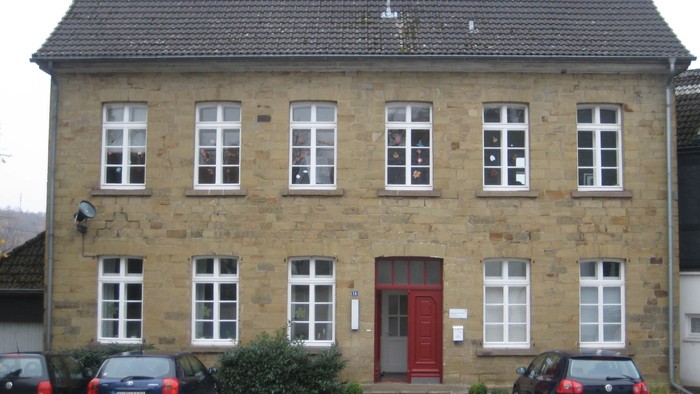 Altes Steinhaus mit rotem Eingang und mehreren geparkten Autos davor