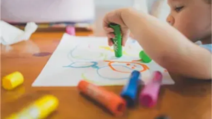 Ein kleines Kind malt kreativ mit bunten, leuchtenden Wachsmalkreiden auf ein Blatt Papier.