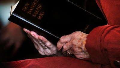 En person holder en dansk bibel med titlen *"Dansk Salmebog"*, mens vedkommende har en rød frakke på.