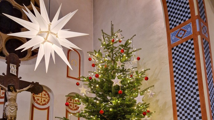 Elegant geschmückter Weihnachtsbaum in einer Kirche mit roten Schmuckstücken, Sternen und funkelnden Lichtern.