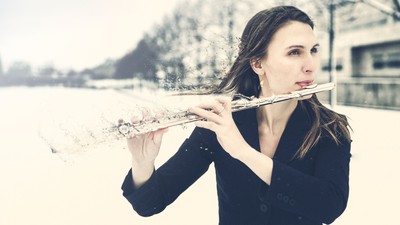 En kvinde spiller fløjte udendørs i et sneklædt, roligt vinterlandskab.