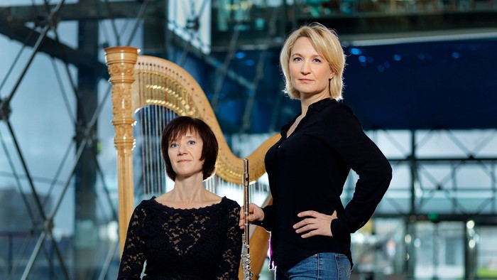To kvinder poser med en stor harpe i en industrielt inspireret, moderne indretning.