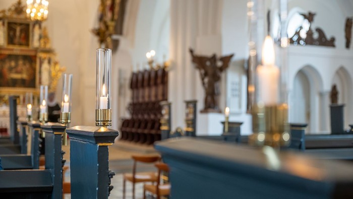 Indre del af en kirke med blå bænke og lysende kandle.