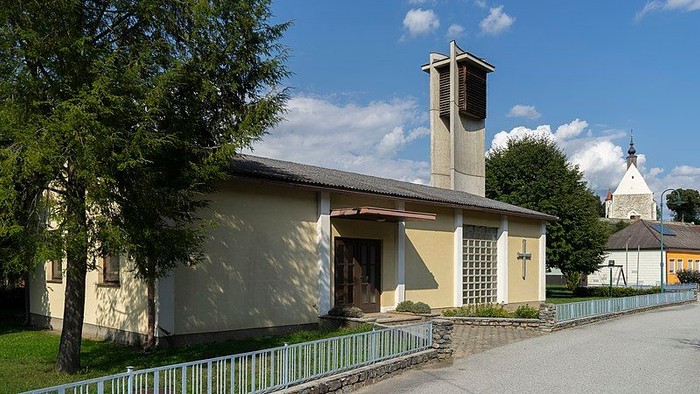 Kleine Kirche mit Glockenturm und grünem Zaun vor blauem Himmel