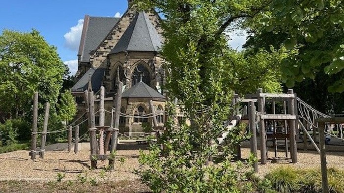 Ein hölzernes Kirchlein mit spitzem Turm in einem grünen Garten