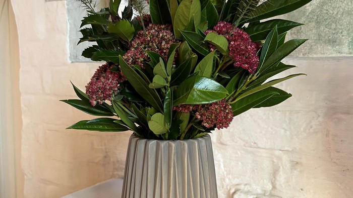 En blomsterstang i en sølvfarvet vase på bord.