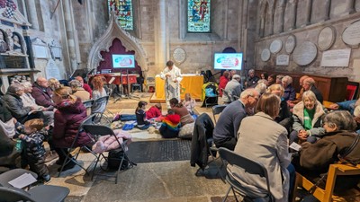 Church interior with people seated, stained glass windows, and a speaker.