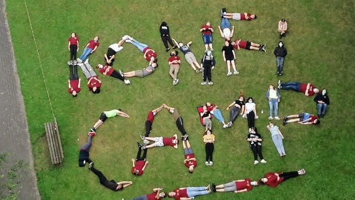 Eine Gruppe von Menschen, die auf dem Gras liegen und mit ihren Körpern das Wort „LOVE“ bilden.