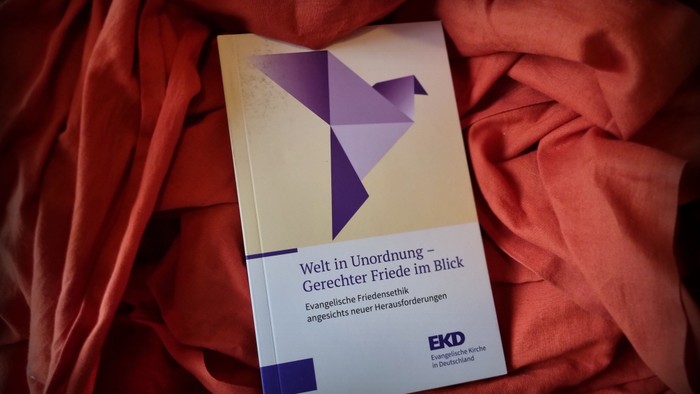 Printausgabe der neuen Friedensdenkschrift der EKD (2025) vor rotem Hintergrund