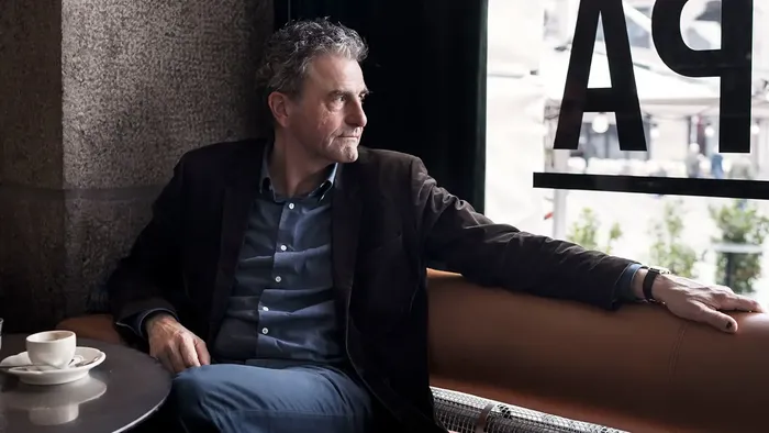 En mand sidder eftertænksomt på en cafébænk med en kop kaffe og kigger ud på gaden.