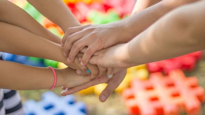 Viele Hände bilden ein Gebinde, farbenfrohe Puzzleteile im Hintergrund