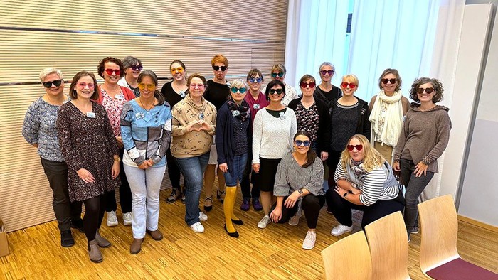 Eine fröhliche Gruppe von Frauen, die drinnen gemeinsam posieren und lässige sowie festliche Kleidung tragen, wobei einige Sonnenbrillen tragen.