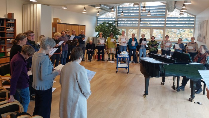 En gruppe af mennesker deltager i en sangstund i et rum med piano.