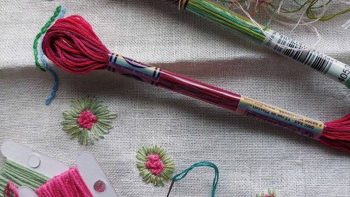 Billedet viser forskellige trådefarver og håndarbejde på stoffet